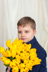 Portrait of a young, beautiful boy. Holds a huge armful of fresh yellow tulips. The concept of spring and holiday, March 8, International Women's Day