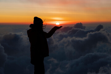 Young woman on top of the mountain holding the sun with her hand during sunset-concept achievement...
