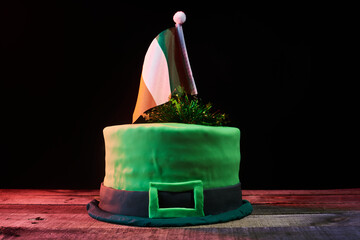 green frosting cake shaped like a green hat with an Irish flag on top, to celebrate St. Patrick's Day. Natural wood base