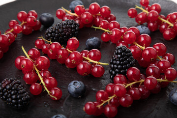 Fresh red currant, blueberries and dewberries on handmade black clay plate