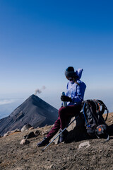 Climber resting with her backpack on the top of the Acatenango volcano observing the volcano of fire in Guatemala-woman hiker climbing the mountain-concept of effort and achievement of goals