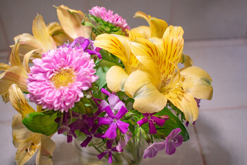 Pink and yellow flower arrangement in a vase. Pink matsumoto asters and yellow alstromeria flowers in a small vase.. Colorful spring flower arrangement indoors.