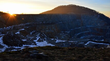 Last rays of winter evening sun above open-cast quarry mine, haulage roads on several stages and...