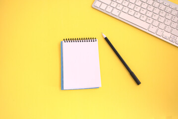 Top view of silver keyboard with notepad and pen on yellow background. Work planning concept.	