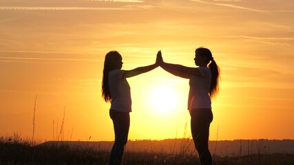 Happy family mom and daughter in field in sun. Mom and daughter touched their palms to each other, hands over a beautiful sunset. Concept of happy family of children and childhood. Mommy daughter