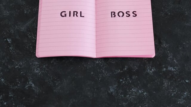equal opportunities Girl Boss text on top of pink notebook on black background