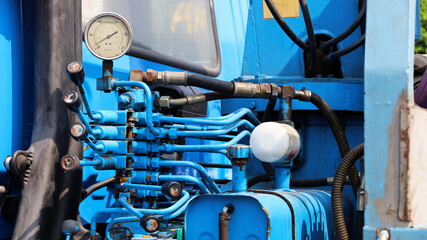 Fototapeta premium Hydraulic control lever and oil gauge. Crane steering levers and blue hoses on a large truck complete with a hydraulic oil tank. Select content and turn off focus.