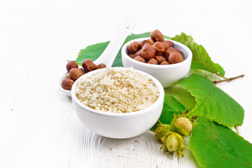 Flour and hazelnuts in bowls on wooden board