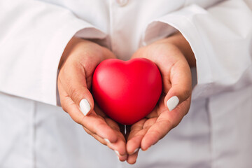 A female doctor wearing a lab coat while holding a red heart in her hands 