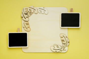 blank square wooden board with wooden leaves shapes decor and black boards on yellow background with copy space