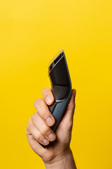 Close up on hand of unknown caucasian man holding electric beard trimmer cordless hair cutter in front of modern yellow background