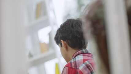 Reflection in mirror of joyful cute Middle Eastern boy talking in slow motion and smiling. Portrait of happy child at home indoors. Lifestyle concept.