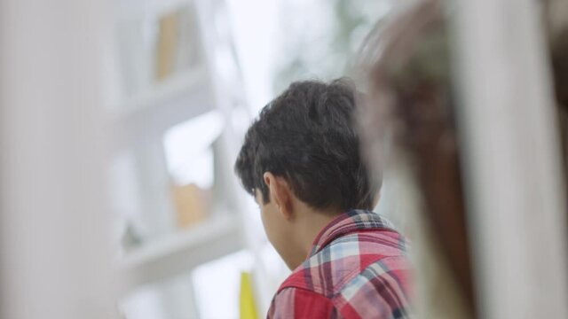 Reflection in mirror of joyful cute Middle Eastern boy talking in slow motion and smiling. Portrait of happy child at home indoors. Lifestyle concept.