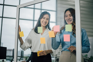 Asian two woman smiling and using post it notes to share about project.