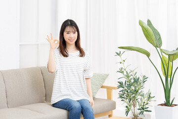 ソファーに座ってOKのジェスチャーをする若い女性