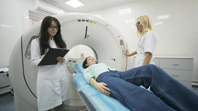 Female patient is undergoing CT or MRI scan under supervision of two qualified radiologists in modern medical clinic. Patient lying on a CT or MRI scan table, moving outside the machine