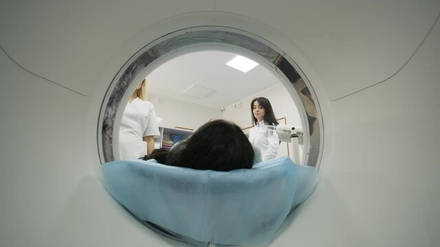 Female patient is undergoing CT or MRI scan under supervision of a radiologist in modern medical clinic. Patient lying on a CT or MRI scan bed, moving inside the machine.