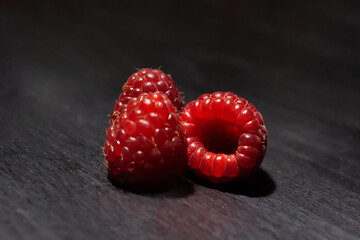 three ripe red raspberries on a dark wooden background close-up