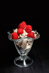 delicious dessert ice cream with raspberries in a transparent cream bowl on a black background close up