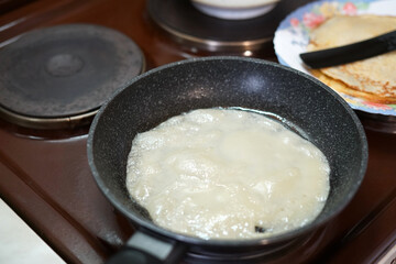 We prepare pancakes in a frying pan at home on an old stove. In a frying pan, batter and a plate of ready-made pancakes.