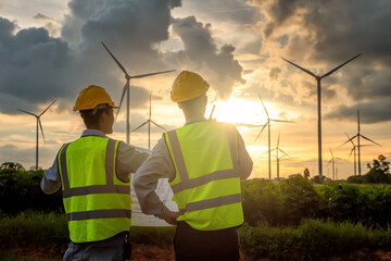 two asian male engineers checking wind turbines during beautiful sunset. Renewable energy...