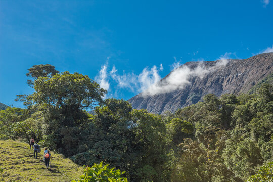 Bajos del Toro, Alajuela, Costa Rica. Group of young adventurers walking through the green field heading to the mountain in the middle of a sunny day and blue summer sky