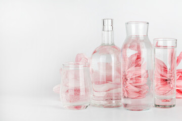 pink flowers distorted through water in glasses and bottle on white background. Home decor, eco friendly, relax, gardening concept. copy space