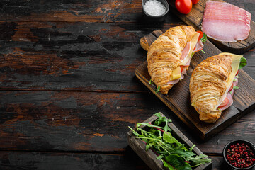 Croissant sandwich with prosciutto, tomatoes, cheese, with herbs and ingredients, on old dark  wooden table background, with copy space for text