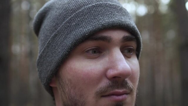 Close-up Portrait of a Young Man in a Knitted Hat on a Blurred Forest Background. Travel Concept, Hicking. Traveler On The Background Of The Forest.