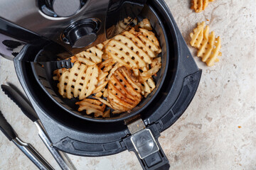 Close up flat lay image of an air fryer oven on kitchen countertop. This offers fast and easy crispy food with little or no fat by circulating hot air inside the basket. A healthy snack alternative.
