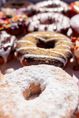 Flat lay image of fresh made store bought donuts in paper box fresh out of the donut shop. An assortment with different flavors and toppings are packed together on flat box, a sweet summer treat