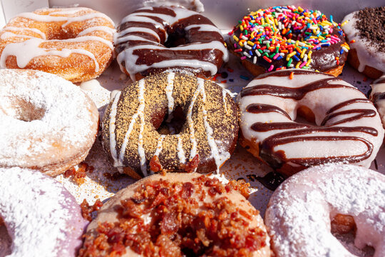 Flat lay image of fresh made store bought donuts in paper box fresh out of the donut shop. An assortment with different flavors and toppings are packed together on flat box, a sweet summer treat