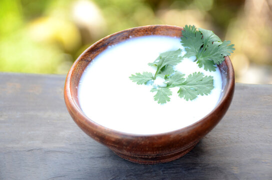 the white yogurt with coriander in the wooden bowl on the green brown wooden background.