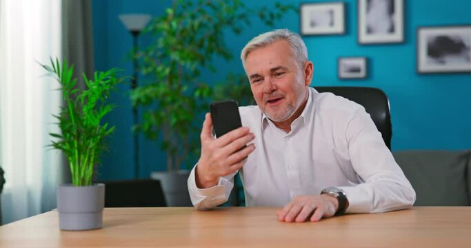 Old middle aged man having video chat using smartphone chatting to son on mobile phone screen smiling enjoying conversation sharing lifestyle with family