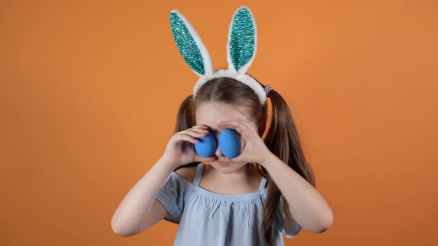 Happy Easter. Little caucasian girl with rabbit ears on her head closes her eyes with two