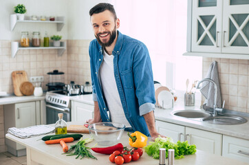 Bearded smiling handsome man in the kitchen at home is posing and looking on the camera