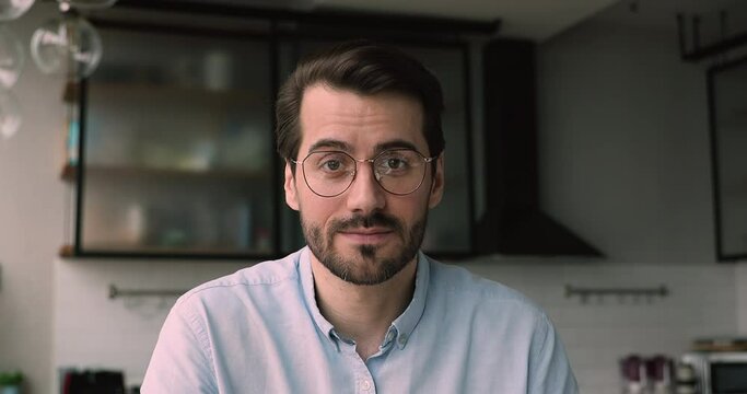 Head shot handsome young man in eyeglasses enjoying web camera call conversation with friends or colleagues. Skilled male blogger recording educational video for followers, sharing knowledge at home.