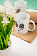 a cup with a drawing of eyes next to a pot of flowers