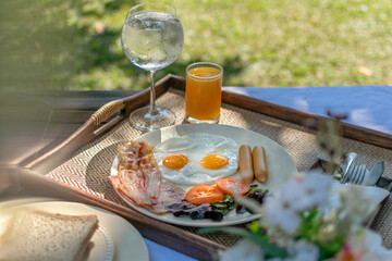 Fresh and delicious breakfast outdoor in the morning with sunny side up eggs, bacon, toast, sausages and juice at the resort in Chiangmai, Thailand. Green grasses visible in the background