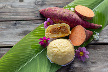Orange sweet potato carrot  yellow steamed bun hand made on banan leaf ,Cosmos flower is decoration wood table top view 