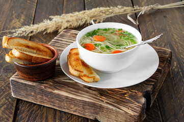 traditional chicken soup with noodles ans carrots served in a bowl over wooden background
