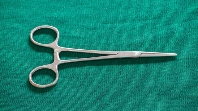 Isolated Hemostatic Forceps scissor on a green-clothed tabletop.