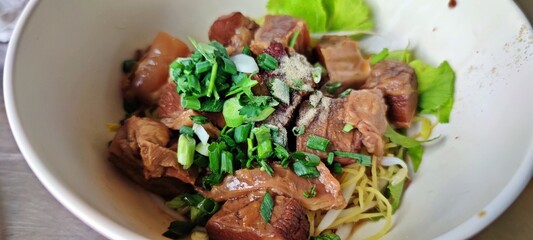Dried egg noodles with Thai braised beef (Thai Stewed) in white bowl.