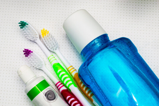 three colorful toothbrushes a tube of toothpaste and a mouthwash lie on the bathroom table close up