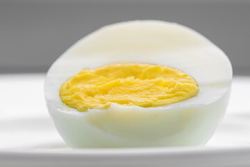 Half of boiled egg with bright yellow egg on white plate on kitchen table.