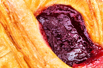 Big fresh yellow croissant with sweet rasberry jam closeup macro view.
