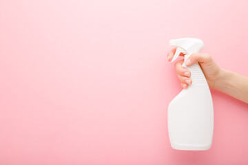 Young adult female hand holding white spray bottle. Detergent for different surfaces in kitchen, bathroom and other rooms. Closeup. Empty place for text or logo. Light pink background. Pastel color. - obrazy, fototapety, plakaty