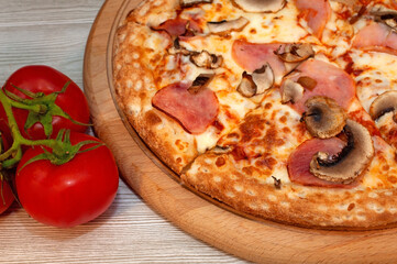 Pizza with ham, mushrooms and cheese on a board with tomatoes