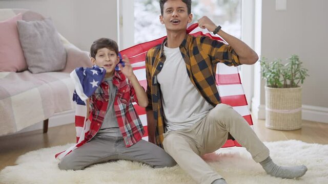 Wide shot of excited sport fans watching match at home with American flag and rejoicing victory. Portrait of Middle Eastern boy and teenager cheering for football or soccer team indoors. Lifestyle.