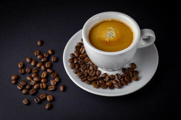 White cup of black coffee with coffee beans around. Black background.